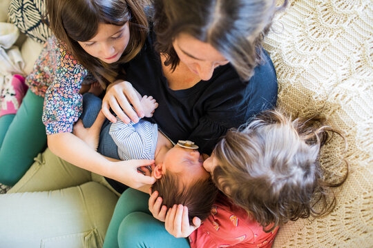 High angle view of mother holding her newborn with daughters on couch.