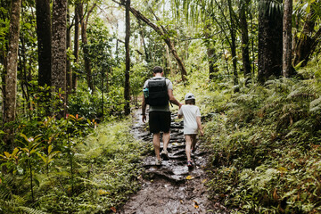 Father helps daughter up a hill while hiking in Hawaiian forest
