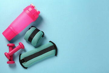 Turquoise weighting agents, dumbbells and shaker on light blue background, flat lay. Space for text