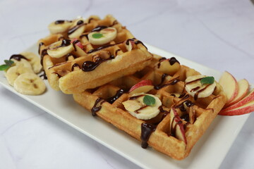 Breakfast waffles with bananas, chocolate spread, apples and toasted almonds. Front view