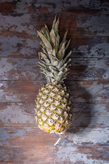 An overhead view of a large, ripe, whole pineapple with a dense green top of short leaves, on a vintage table with shabby paint. Useful properties of pineapple. Vertical orientation