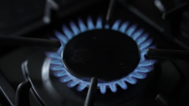 High Angle View Blue Flame On Gas Burner Of Kitchen Stove. Close-up Natural Gas Burning Indoors On Black Cooking Stove Top