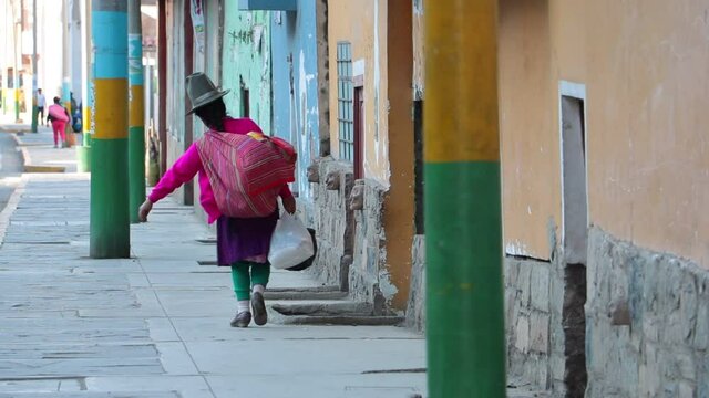 Traditionally dressed Peruvian woman walks through the street of an andean village with a lot of luggage.