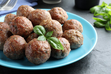 Tasty cooked meatballs with basil on black table, closeup