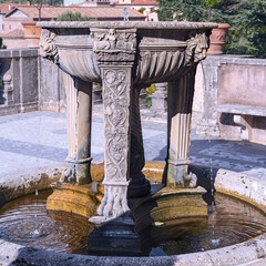 an ancient fountain in the form of a stone bowl with lion heads around the edges in the suburbs of the Italian capital