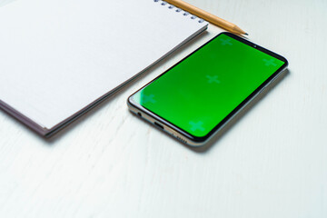 White blank notepad smartphone green screen mockup and pencil flat lay. Tamplate for design