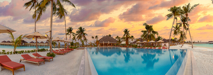 Fantastic panoramic poolside, sunset sky, palm trees. Luxury tropical beach landscape, infinity swimming pool, deck chairs loungers under umbrellas amazing scenic. Vacation resort hotel landscape