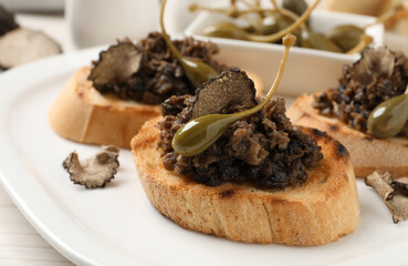 Delicious bruschettas with truffle sauce and caperberries on white plate, closeup