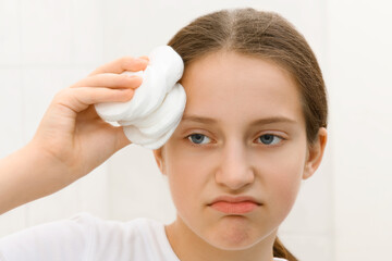 face of a teenage girl, she looks at herself in the mirror and takes care of her skin, does...