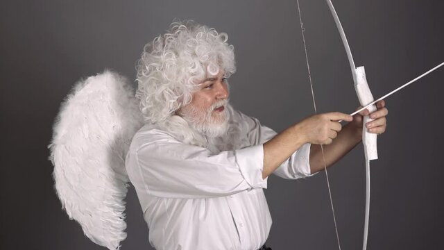 Crazy angel cupid valentin with bow arrow ready to shoot. Funny bearded man with feathers wings of Cupid Valentines Day.