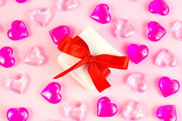 Top view of small white wrapped gift box with bright pink hearts and on light rose background. Valentines day, Birthday, Mothers day surprise present.