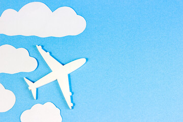 White plane model on light sky blue background with paper clouds and copy space top view flat lay.