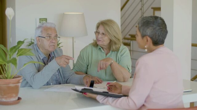 Senior couple talking with realtor while sitting at table. Elderly man and women in eyeglasses having negotiations with real estate agent, discussing details of agreement. Real estate purchase concept