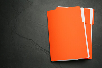Orange files with documents on black slate table, top view. Space for text