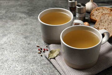 Hot delicious bouillon in cups on grey table. Space for text