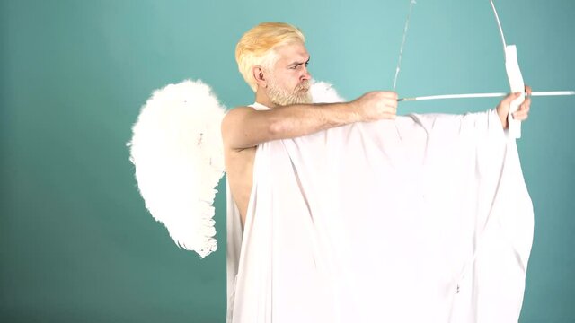 Funny cupid, handsome guy on valentine day with bow arrow shooting. Love concept. Handsome crazy fun angel. Bearded angel valentin man with angel wings. Valentines Day. Humor comical concept.