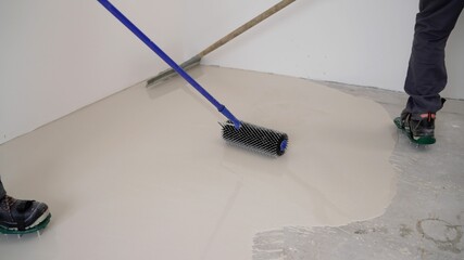 The concept of self-leveling floors. Worker puts primer on concrete floor. Applying a primer to a...