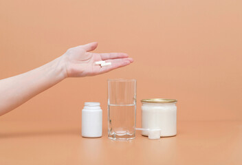 Hand holds a collagen pill on a beige background. Hydrolyzed collagen protein powder in a jar and a glass of water. Concept of a healthy lifestyle.