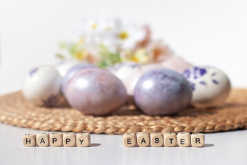 Easter concept. Purple eggs on a straw cloth and wooden letters happy Easter