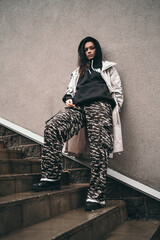 Naklejka premium An upset girl stands against a wall on the street. A girl in a black hoodie. Space for text. A teenager in a black hood is offended. 