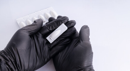 Hands in black gloves  opens suppositories for anal or vaginal use. Medical candles for the...
