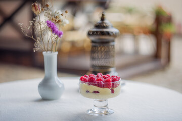 Dessert of fresh raspberries and cottage cheese in a glass cup, a vase with flowers and a candlestick on a white background. Vintage oriental interior. Oriental-style cafe