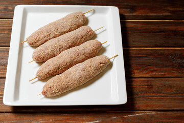 There are four sausages with sticks in it on the wood table.