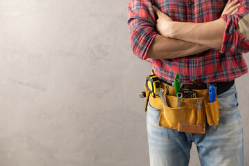 Worker man with tool belt near concrete or cement wall. Male hand and tools for house renovation - obrazy, fototapety, plakaty