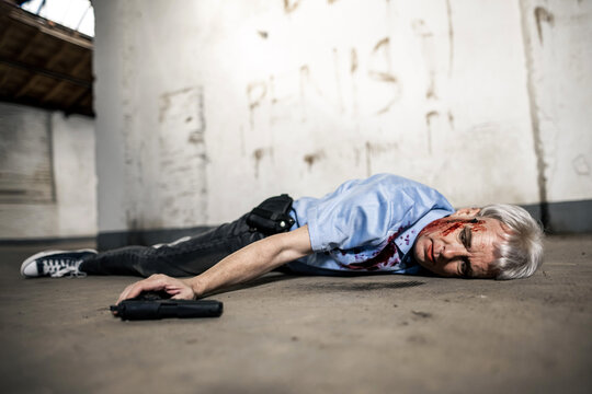 Ein Mensch hat sich mit einer Pistole selbst getötet und liegt blutend und mit aufgerissenen Augen auf dem Betonboden. 