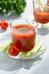 Two glasses with fresh tomato juice, celery, parsley and ripe tomatoes on light background