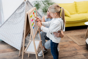 Parent hugging child and pointing at magnetic easel at home.