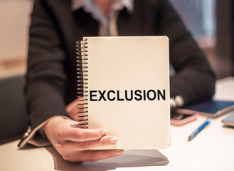 Woman at her working place holds the notebook with the text EXCLUSION