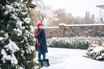 Young woman cleans snow in the yard in snowy weather.