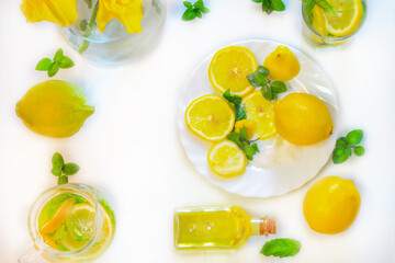 Flat lay of lemon fruit, mint leaves and sprigs and lemon drink in a jug and bottles of lemon oil shot in natural light. Useful healthy fresh drink drink with mint and lemon.