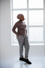 Fototapeta na wymiar Attractive african american woman in headscarf and casual clothes standing in studio with white background and looking at window. Concept of people and lifestyles.