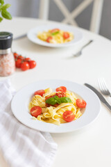 Italian pasta with cherry tomatoes, tomato sauce and cheese, garnished with a sprig of basil. Ready lunch or dinner. Table setting