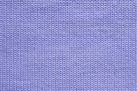 Texture of blue violet wool knitted sweater close-up. Abstract stockinette fabric background in trendy color of the year 2022 very peri. Design element for warm handmade clothing concepts.