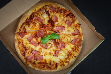 Round baked pizza in a craft box on a black