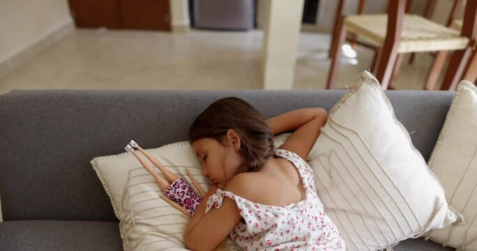 Cute little girl sleeping on gray sofa with white pillows