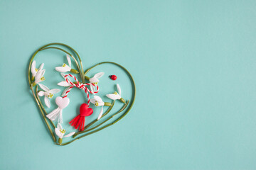 Green and turquoise background with a heart of snowdrops and red and white rope with tassels. Postcard for the holiday on March 1, Martisor, Baba Marta. - 481046439