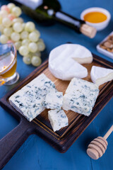 appetizer assorted cheese dor blue and camembert on a wooden board with honey and grapes and with a bottle  of wine