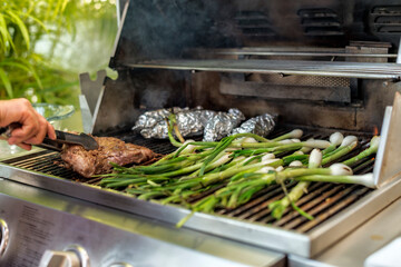Spring onions and meat being roasted on the grill using metal tongs
