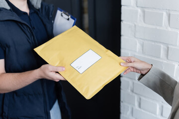 Cropped view of businesswoman taking parcel from courier with clipboard in office. - obrazy, fototapety, plakaty