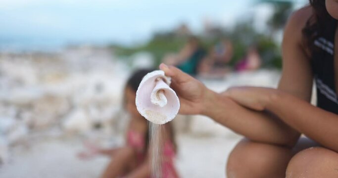 Hand pouring sand from conch shell with blurry background