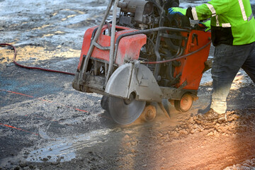 Worker using an asphalt saw cutting machine in winter