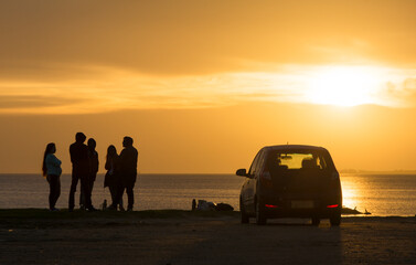 Amigos conversando encuentro en la costa, hora dorada en atardecer con un auto estacionado
