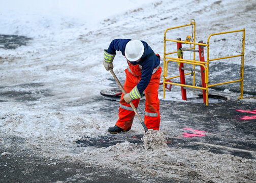 Unidentified worker shovelling snow near open manhole