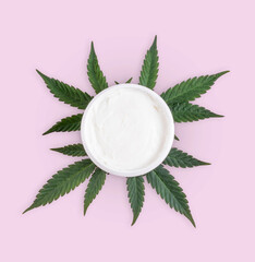 Marijuana cannabis cemp plant leaf next to a container of face cream or lotion. Isolated on pink...