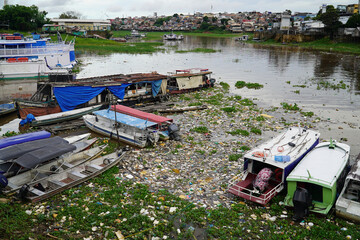 Fototapeta na wymiar Plastic waste pollution. The Rio Negro river near the metropolis of Manaus. Garbage in the river banks between boats, ships and houseboats. Manaus, Amazon region, Brasil