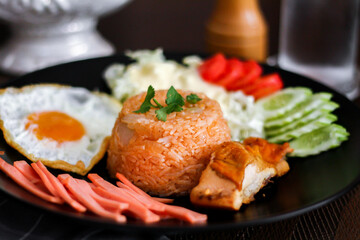 Fried rice, fried egg, cucumber, sliced tomato, green salad and Fried chicken placed on a black plate as a garnish.